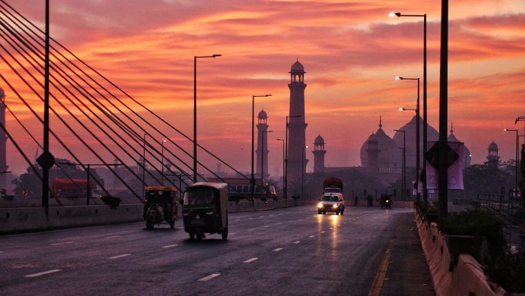 Vehicles driving on a bridge with a mosque and sunset in the background.